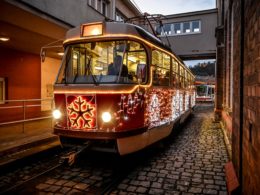 Ozdobená tramvaj s vánoční výzdobou jede po kolejích ve večerním městském prostředí.