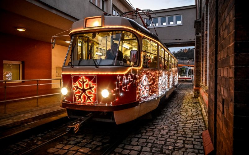 Ozdobená tramvaj s vánoční výzdobou jede po kolejích ve večerním městském prostředí.