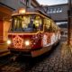 Ozdobená tramvaj s vánoční výzdobou jede po kolejích ve večerním městském prostředí.