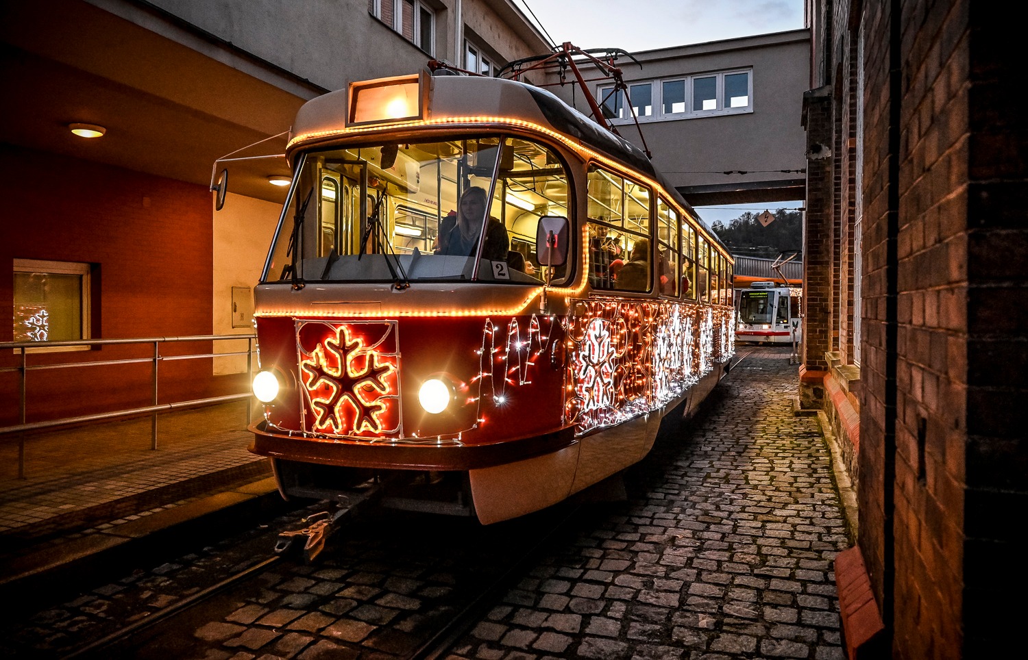 Ozdobená tramvaj s vánoční výzdobou jede po kolejích ve večerním městském prostředí.