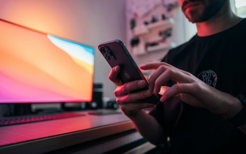 Muž používající iPhone před počítačovým monitorem s barevným gradientem.