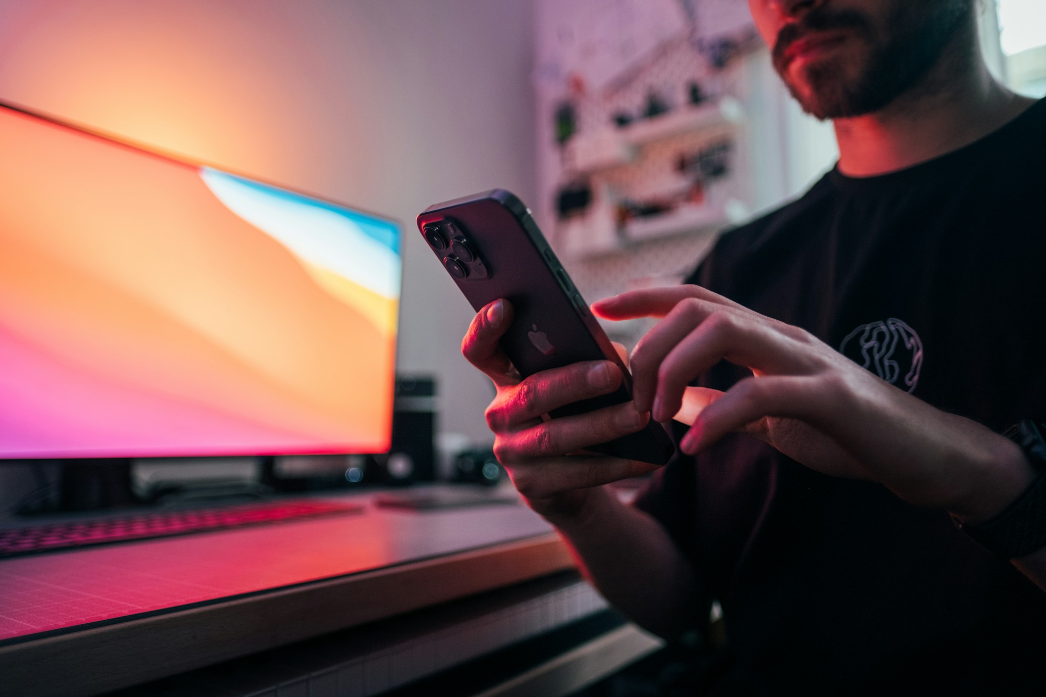 Muž používající iPhone před počítačovým monitorem s barevným gradientem.