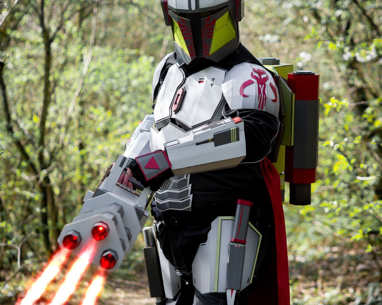 Cosplayer v kostýmu futuristického bojovníka s červenými světelnými meči v lese.