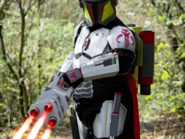 Cosplayer v kostýmu futuristického bojovníka s červenými světelnými meči v lese.