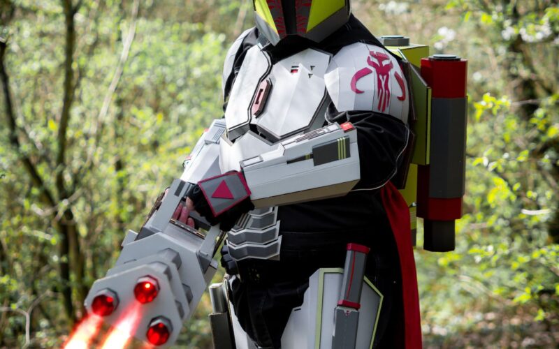 Cosplayer v kostýmu futuristického bojovníka s červenými světelnými meči v lese.