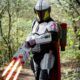 Cosplayer v kostýmu futuristického bojovníka s červenými světelnými meči v lese.