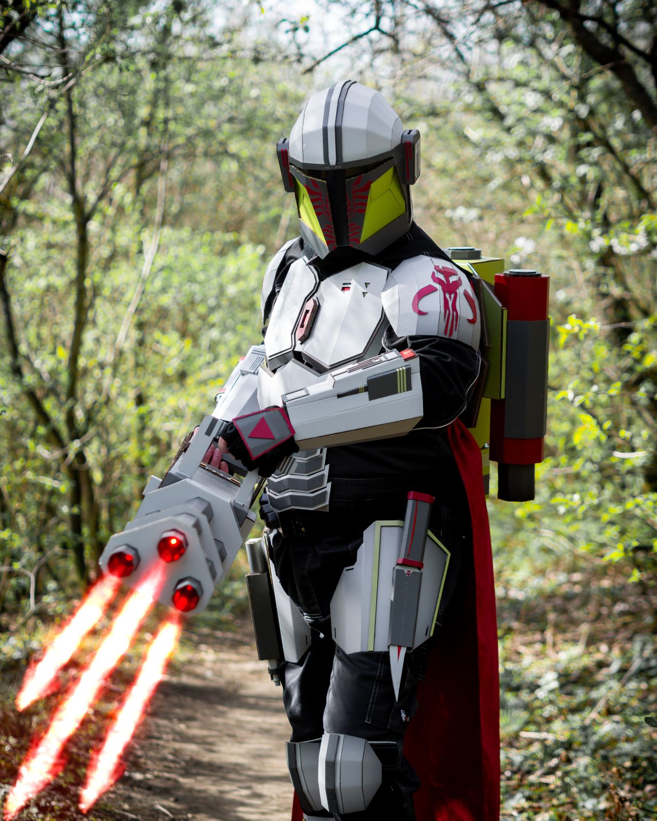 Cosplayer v kostýmu futuristického bojovníka s červenými světelnými meči v lese.