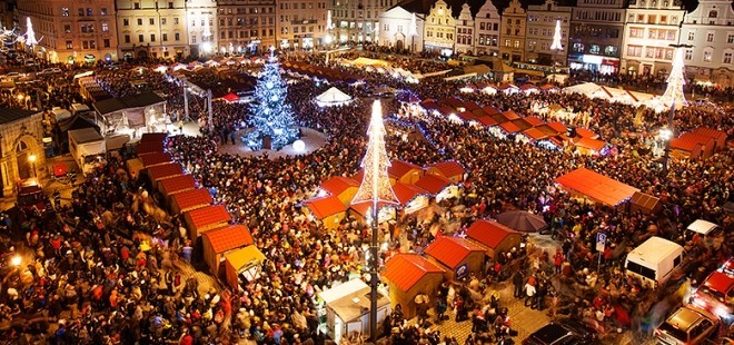 Vánoční trhy s mnoha stánky a velkým ozdobeným stromem na náměstí ve večerních hodinách.