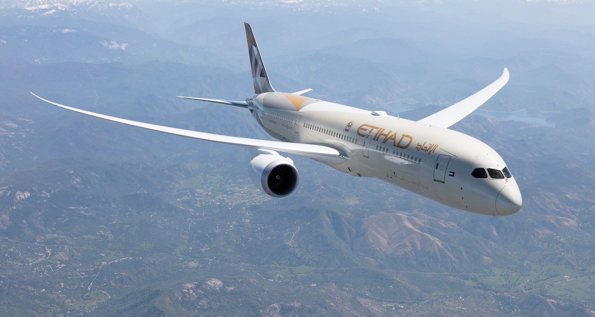 Letadlo společnosti Etihad Airways letí nad krajinou s horami v pozadí.